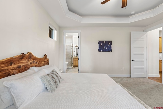 carpeted bedroom with a tray ceiling, connected bathroom, and ceiling fan