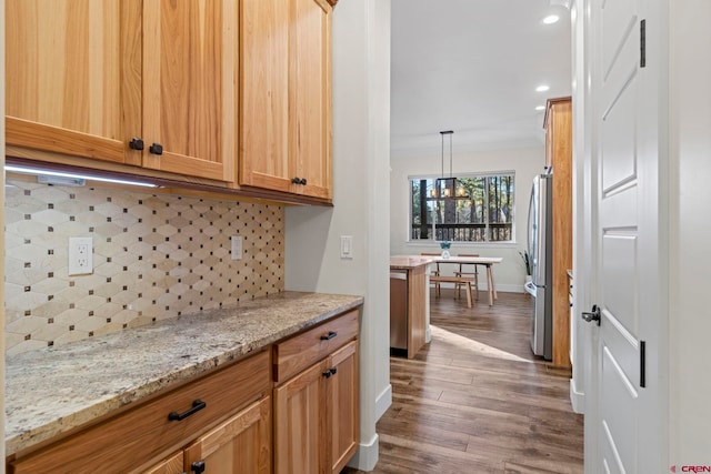 kitchen with hanging light fixtures, decorative backsplash, stainless steel fridge, light stone countertops, and wood-type flooring