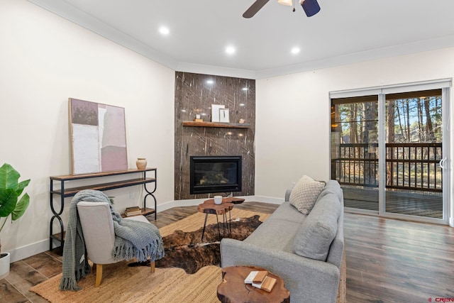 living room featuring hardwood / wood-style flooring, ceiling fan, ornamental molding, and a fireplace