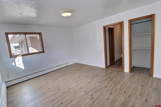 spare room featuring light wood-type flooring, a textured ceiling, and a baseboard heating unit