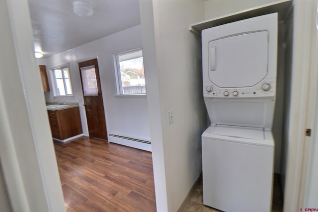 clothes washing area featuring sink, stacked washer and dryer, dark wood-type flooring, and a baseboard heating unit