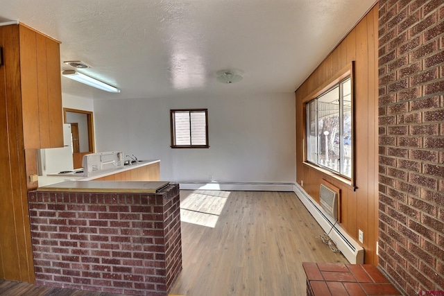 kitchen featuring baseboard heating, kitchen peninsula, light hardwood / wood-style flooring, and brick wall