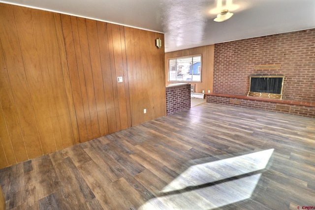 living room featuring wood walls, dark wood-type flooring, a baseboard heating unit, a brick fireplace, and brick wall