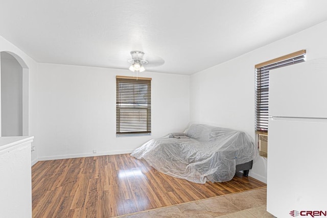 bedroom with wood-type flooring, white fridge, and ceiling fan