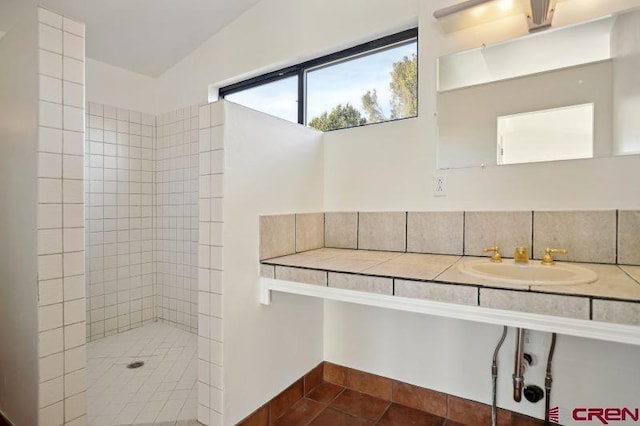 bathroom with tile patterned floors, sink, vaulted ceiling, decorative backsplash, and a tile shower