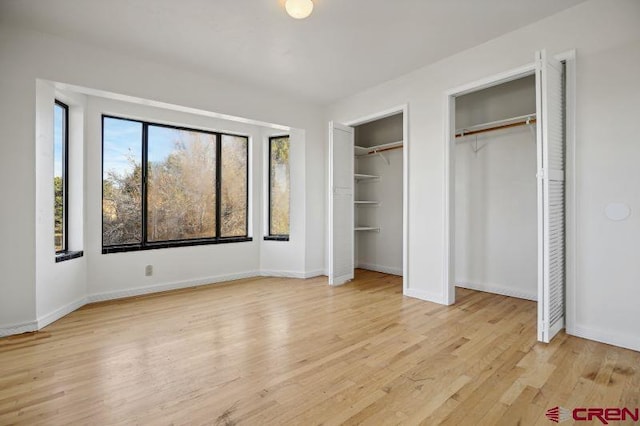 unfurnished bedroom featuring multiple closets and light hardwood / wood-style flooring