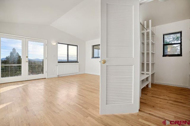 spare room featuring french doors, light wood-type flooring, vaulted ceiling, and radiator heating unit