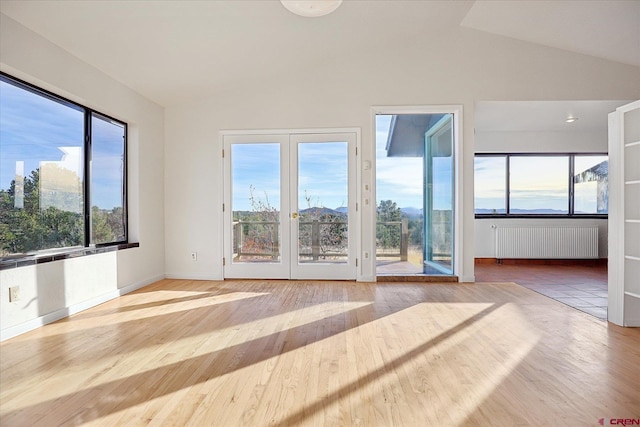 unfurnished living room featuring radiator heating unit, hardwood / wood-style flooring, vaulted ceiling, and a wealth of natural light