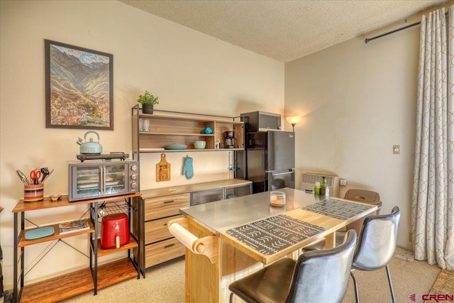 kitchen featuring a breakfast bar, stainless steel fridge, light colored carpet, and a textured ceiling