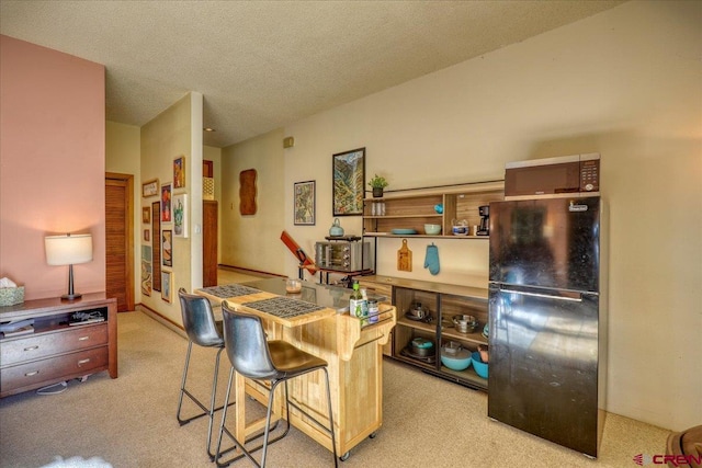 kitchen with a kitchen breakfast bar, a textured ceiling, light colored carpet, and black fridge