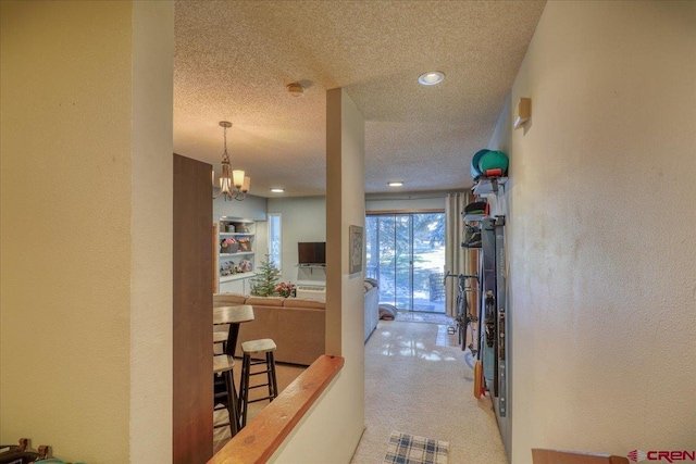 hall featuring light carpet, a textured ceiling, and a chandelier