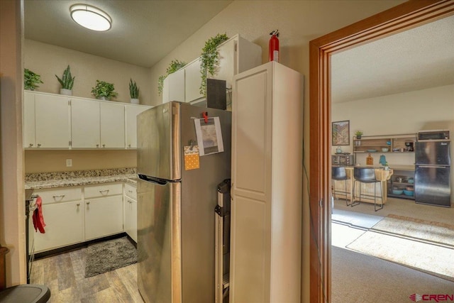 kitchen with white cabinets, black fridge, a textured ceiling, light hardwood / wood-style floors, and stainless steel refrigerator