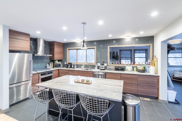 kitchen featuring a wealth of natural light, a center island, wall chimney exhaust hood, and stainless steel appliances