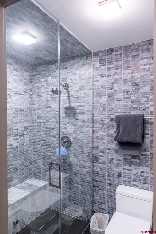 bathroom featuring walk in shower, toilet, and tile walls