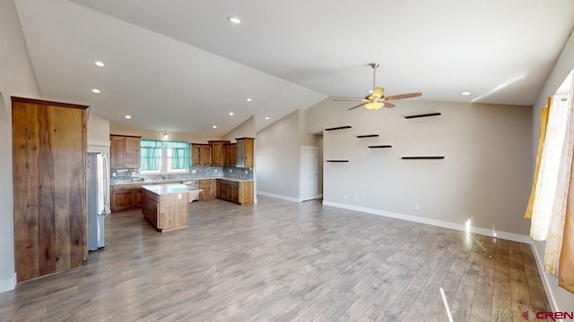 kitchen featuring stainless steel refrigerator, ceiling fan, a center island, backsplash, and hardwood / wood-style flooring