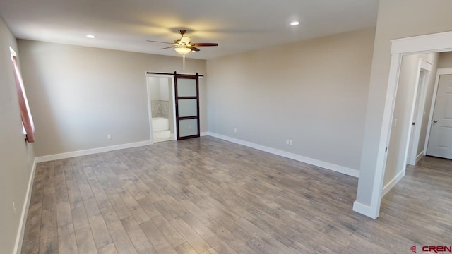 spare room featuring a barn door, light hardwood / wood-style flooring, and ceiling fan