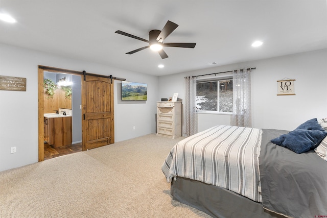 carpeted bedroom featuring a barn door, ensuite bathroom, ceiling fan, and sink