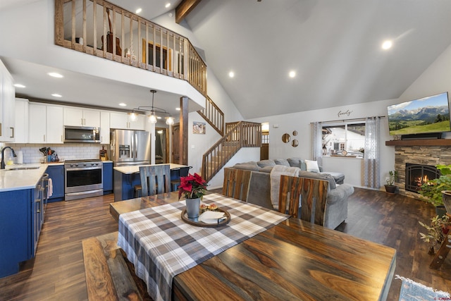 dining area featuring dark hardwood / wood-style flooring, sink, beam ceiling, high vaulted ceiling, and a stone fireplace