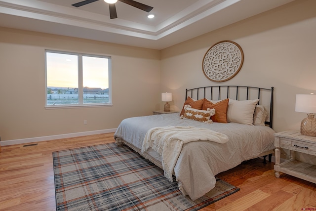 bedroom with a raised ceiling, light hardwood / wood-style flooring, and ceiling fan