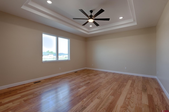 empty room featuring a raised ceiling, ceiling fan, and light wood-type flooring