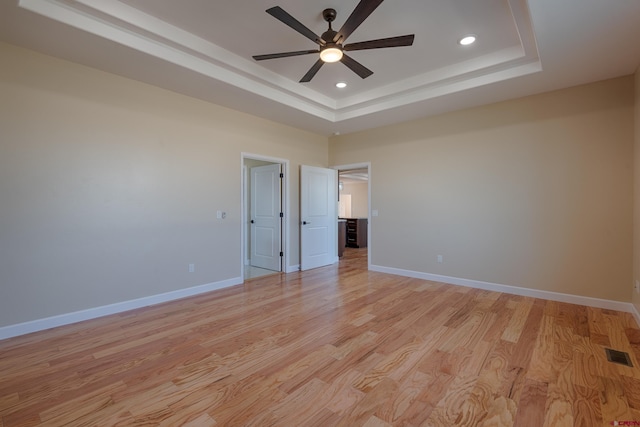 unfurnished bedroom featuring a tray ceiling, ceiling fan, and light hardwood / wood-style flooring