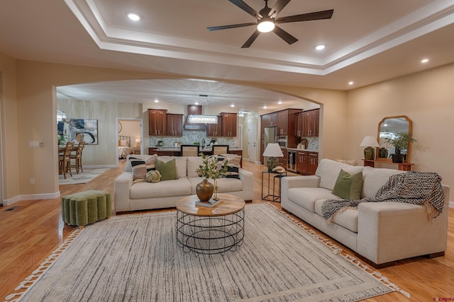 living room with ceiling fan, light wood-type flooring, and a tray ceiling