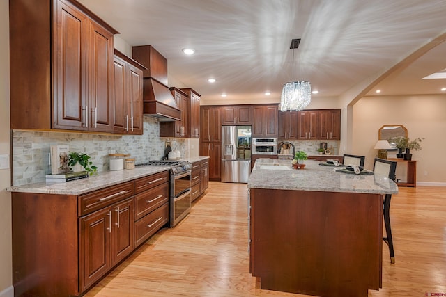 kitchen featuring hanging light fixtures, stainless steel appliances, light hardwood / wood-style floors, a kitchen bar, and a center island with sink