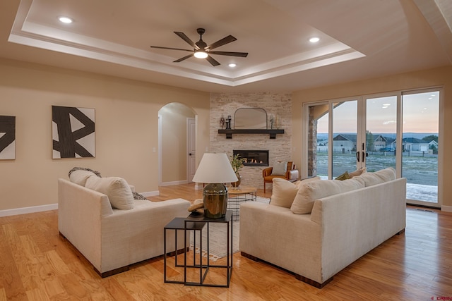 living room featuring a fireplace, light hardwood / wood-style floors, a raised ceiling, and ceiling fan