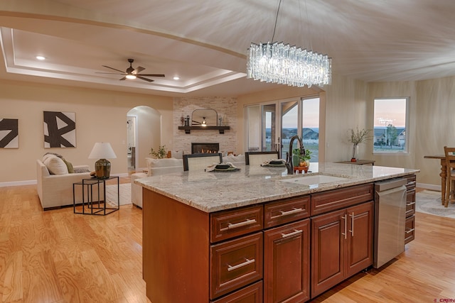 kitchen featuring a kitchen island with sink, ceiling fan with notable chandelier, light hardwood / wood-style flooring, a tray ceiling, and light stone counters