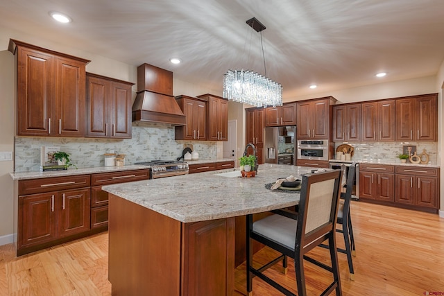 kitchen featuring sink, light hardwood / wood-style flooring, an island with sink, appliances with stainless steel finishes, and custom range hood