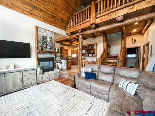 living room featuring beam ceiling, high vaulted ceiling, a stone fireplace, and wood ceiling