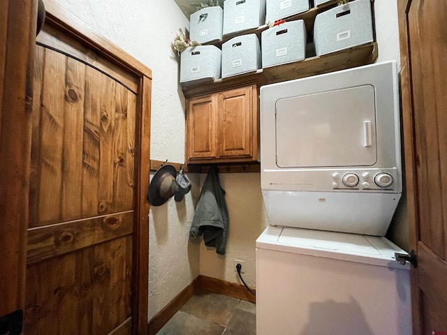 clothes washing area featuring cabinets, stacked washing maching and dryer, and dark tile patterned flooring