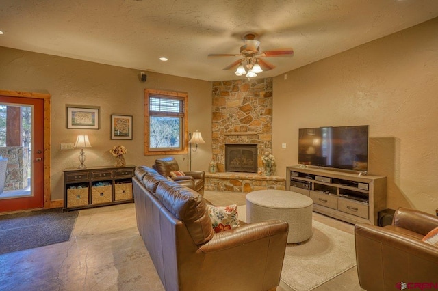 living room with a textured ceiling, a stone fireplace, and ceiling fan