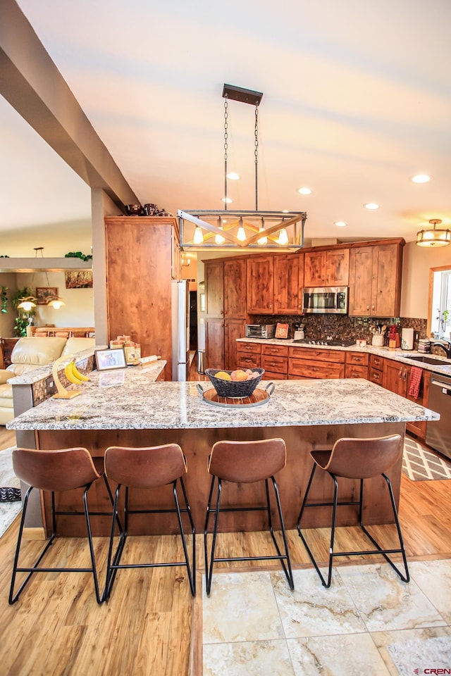 kitchen featuring a breakfast bar area, light wood-type flooring, tasteful backsplash, decorative light fixtures, and stainless steel appliances