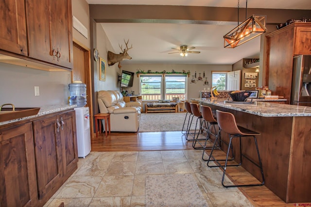 kitchen featuring ceiling fan, light stone counters, light hardwood / wood-style flooring, pendant lighting, and a breakfast bar area