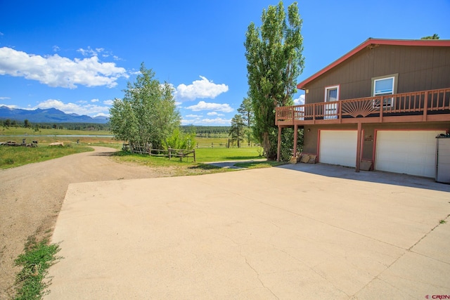 exterior space featuring a deck with mountain view, a rural view, a garage, and a lawn