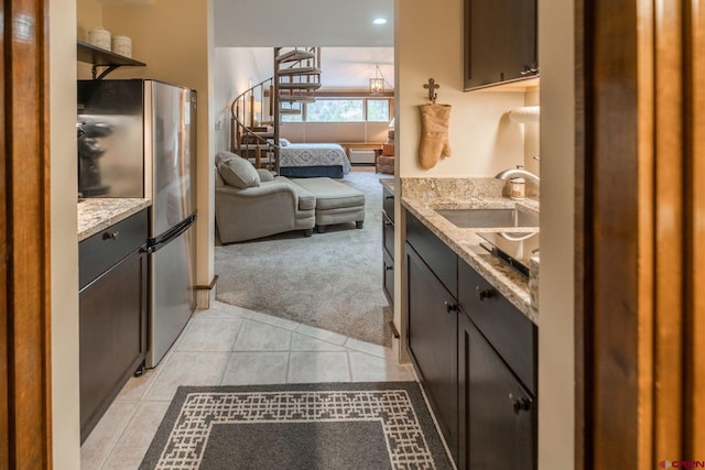 kitchen with light carpet, stainless steel fridge, light stone counters, dark brown cabinetry, and sink