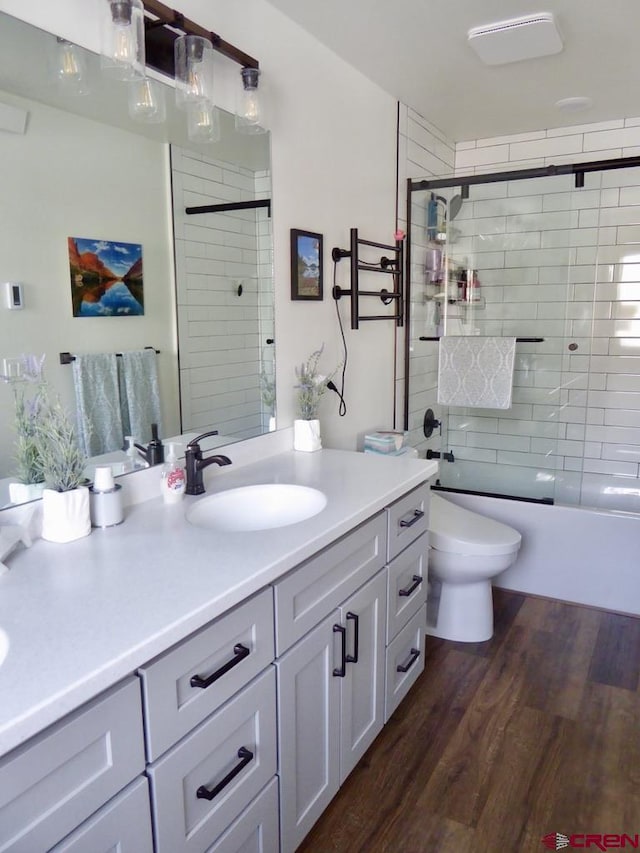 full bathroom with vanity, toilet, wood-type flooring, and bath / shower combo with glass door