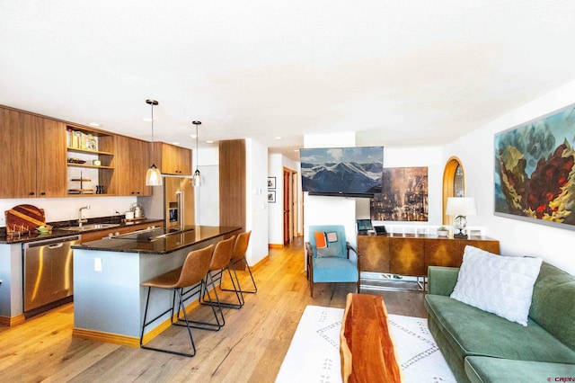 kitchen with sink, light wood-type flooring, decorative light fixtures, a kitchen bar, and stainless steel appliances