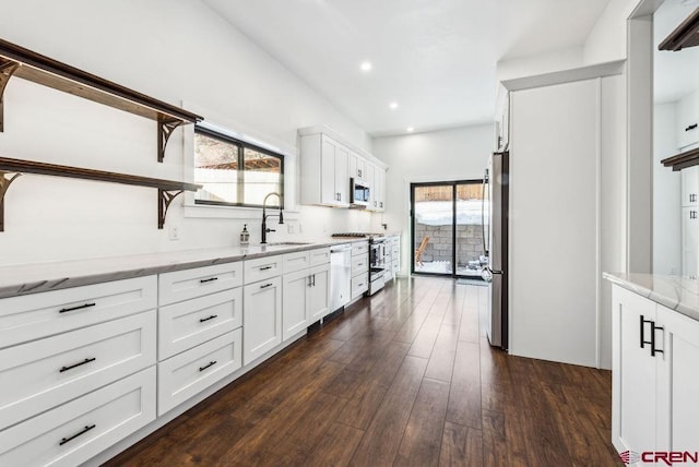 kitchen with appliances with stainless steel finishes, light stone counters, dark wood-type flooring, sink, and white cabinets