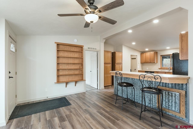 kitchen with lofted ceiling, black fridge, kitchen peninsula, a kitchen bar, and wood-type flooring