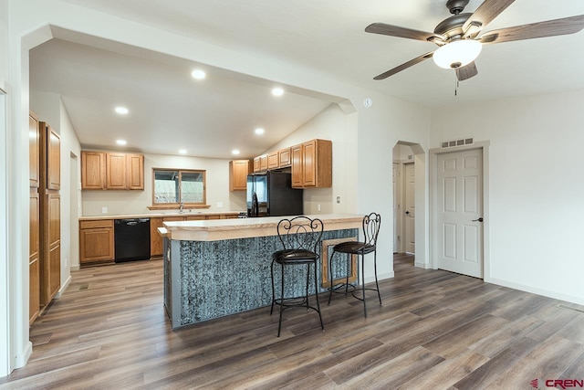 kitchen with a kitchen breakfast bar, kitchen peninsula, black appliances, and hardwood / wood-style flooring