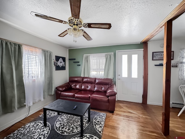 living room featuring wood-type flooring, a textured ceiling, a baseboard radiator, and a healthy amount of sunlight