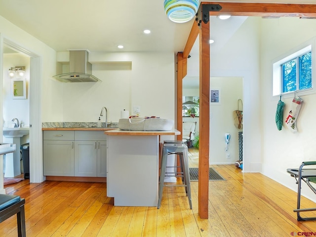 kitchen featuring a kitchen breakfast bar, light hardwood / wood-style flooring, range hood, kitchen peninsula, and gray cabinets