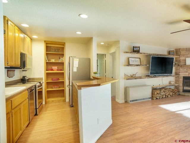 kitchen with stainless steel appliances, light hardwood / wood-style flooring, ceiling fan, and a stone fireplace