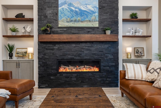 living room featuring built in shelves, a stone fireplace, and light wood-type flooring