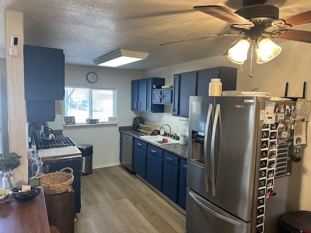 kitchen with sink, blue cabinets, light wood-type flooring, a textured ceiling, and appliances with stainless steel finishes