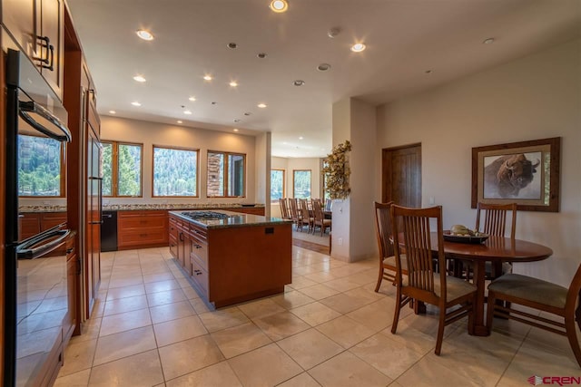 kitchen with a center island, light tile patterned flooring, dark stone countertops, and stainless steel gas cooktop