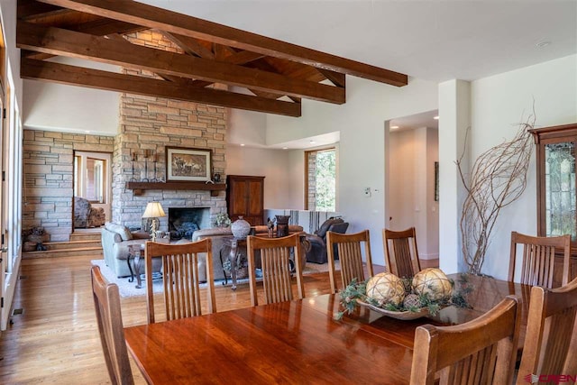 dining area featuring a fireplace, light wood-type flooring, a wealth of natural light, and beamed ceiling