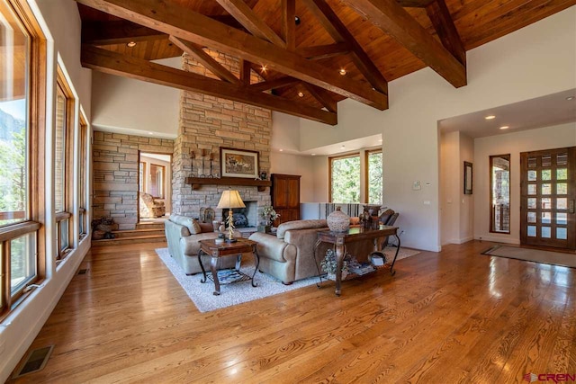 living room with a stone fireplace, high vaulted ceiling, and light hardwood / wood-style flooring